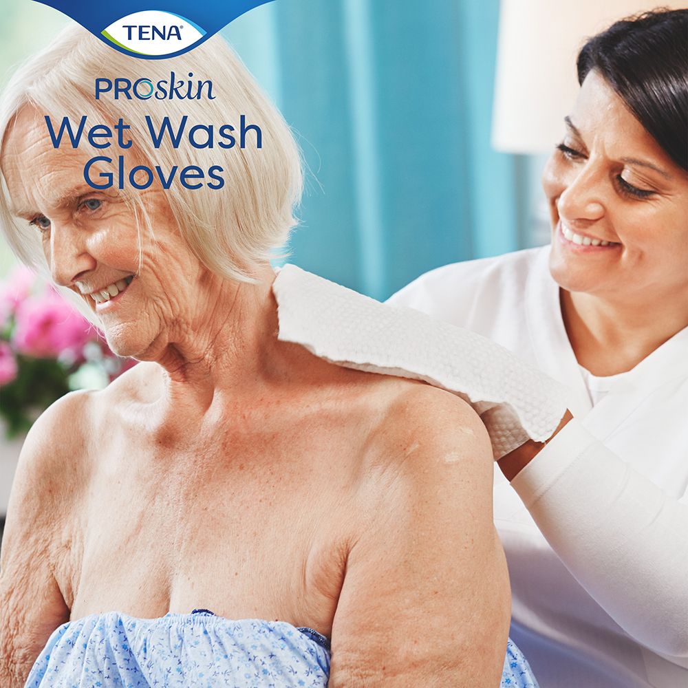 Una donna anziana riceve un Wet Wash Glove da un'infermiera. Nome del prodotto e logo visibili. Guanto bianco.