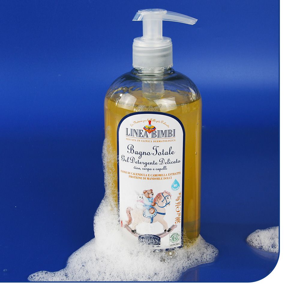 Flacone di gel detergente con dosatore, circondato da schiuma. Scritta: LINEA BIMBI, Bagno Totale, Gel Detergente Delicato. Bambino su cavallo a dondolo.