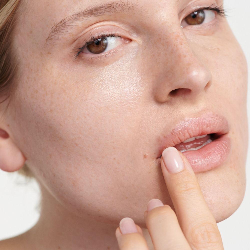 Primo piano di una persona che applica il balsamo per le labbra. Tono della pelle, dita, labbra visibili.