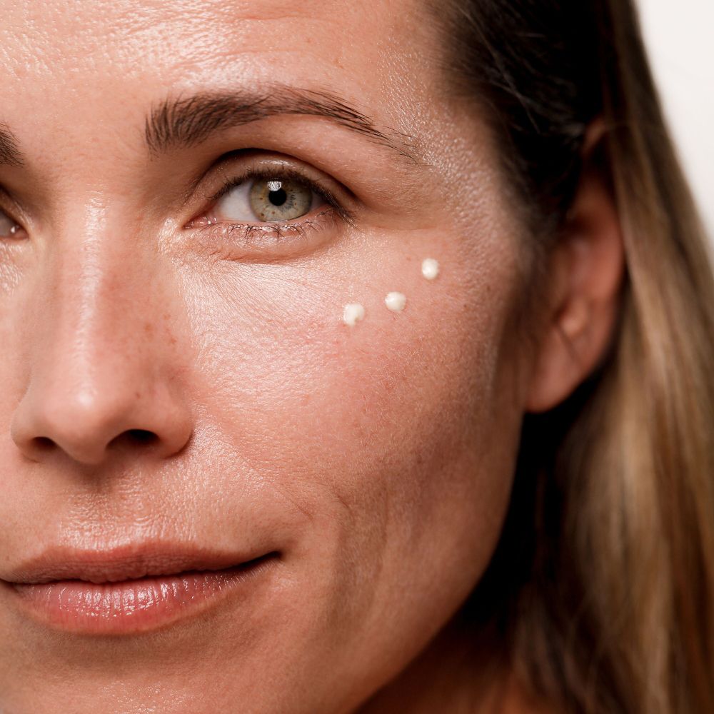 Donna con punti di crema sotto l'occhio. Pelle chiara, capelli biondi.