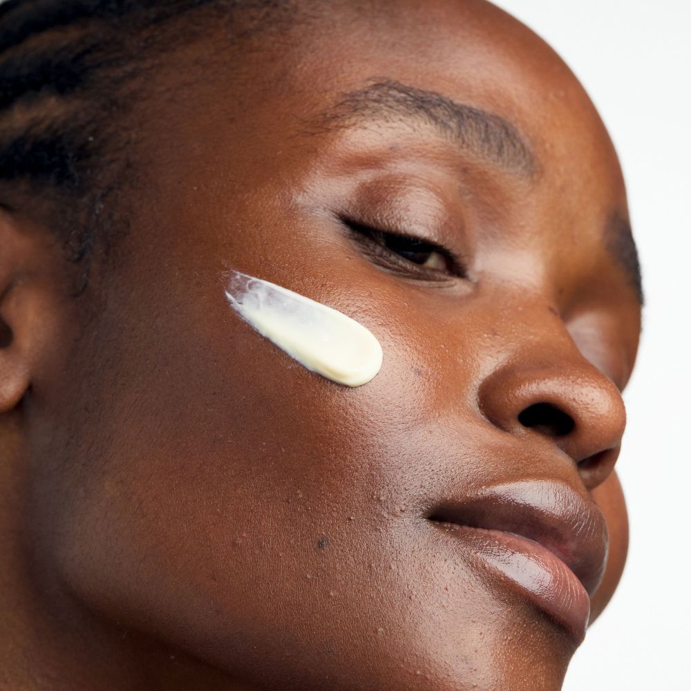 Primo piano di un viso con crema sulla pelle. Tono della pelle: scuro. Occhi chiusi.