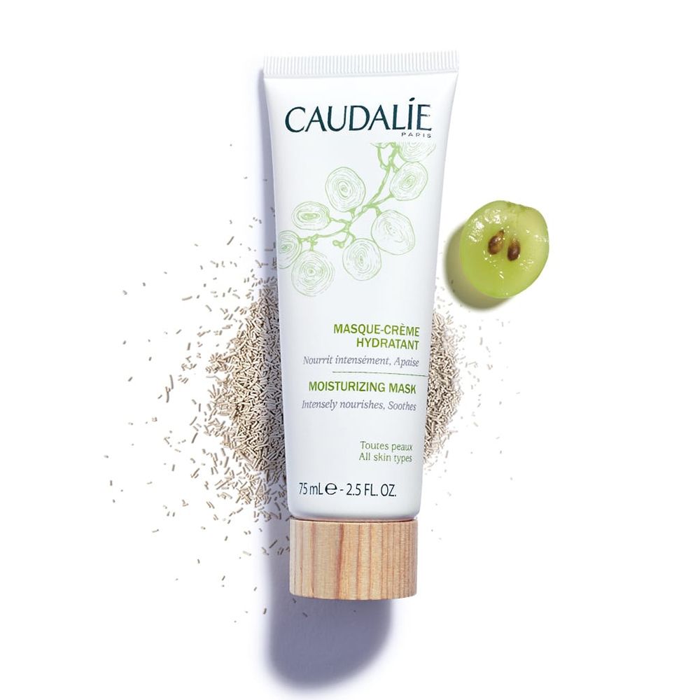 Tubo bianco con stampa verde. Testo: CAUDALIE, MASQUE-CRÈME HYDRATANT, MOISTURIZING MASK. Base in legno. Uva e semi.