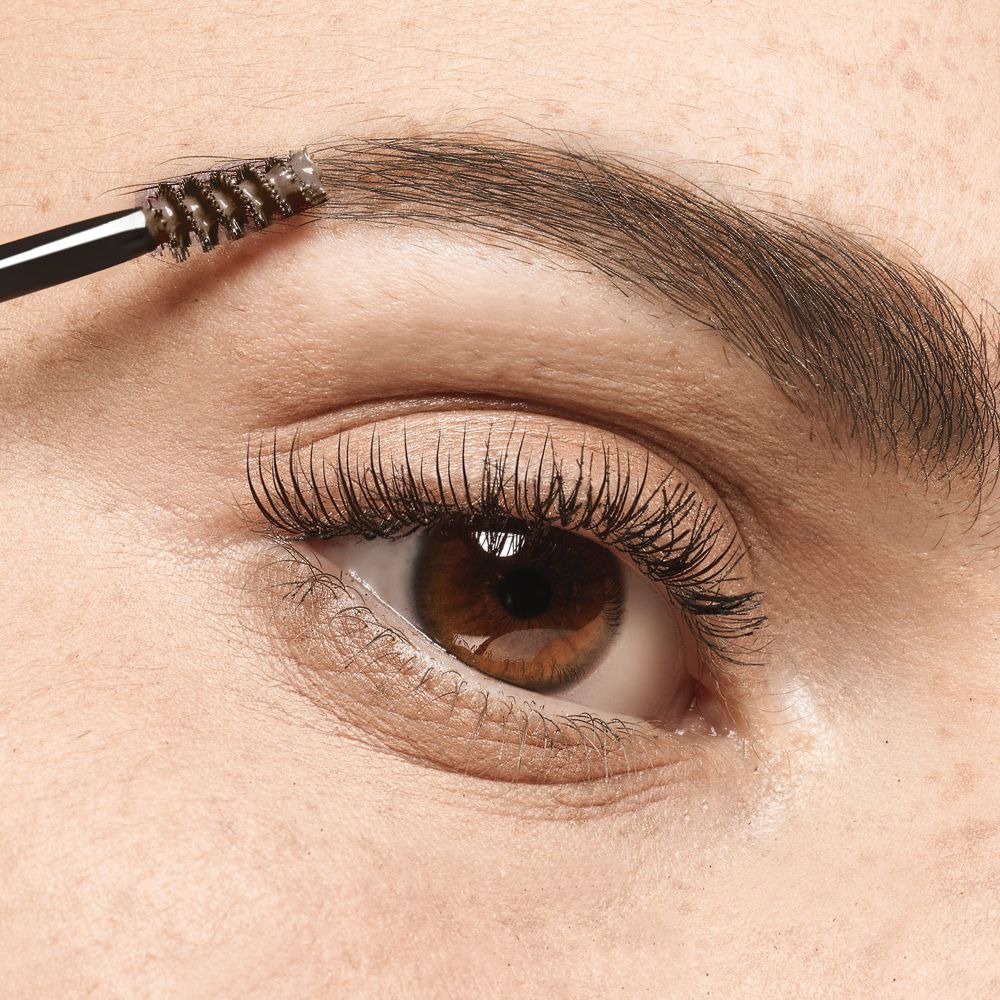 Occhio con sopracciglio spazzolato con un applicatore di mascara. Occhi marroni.