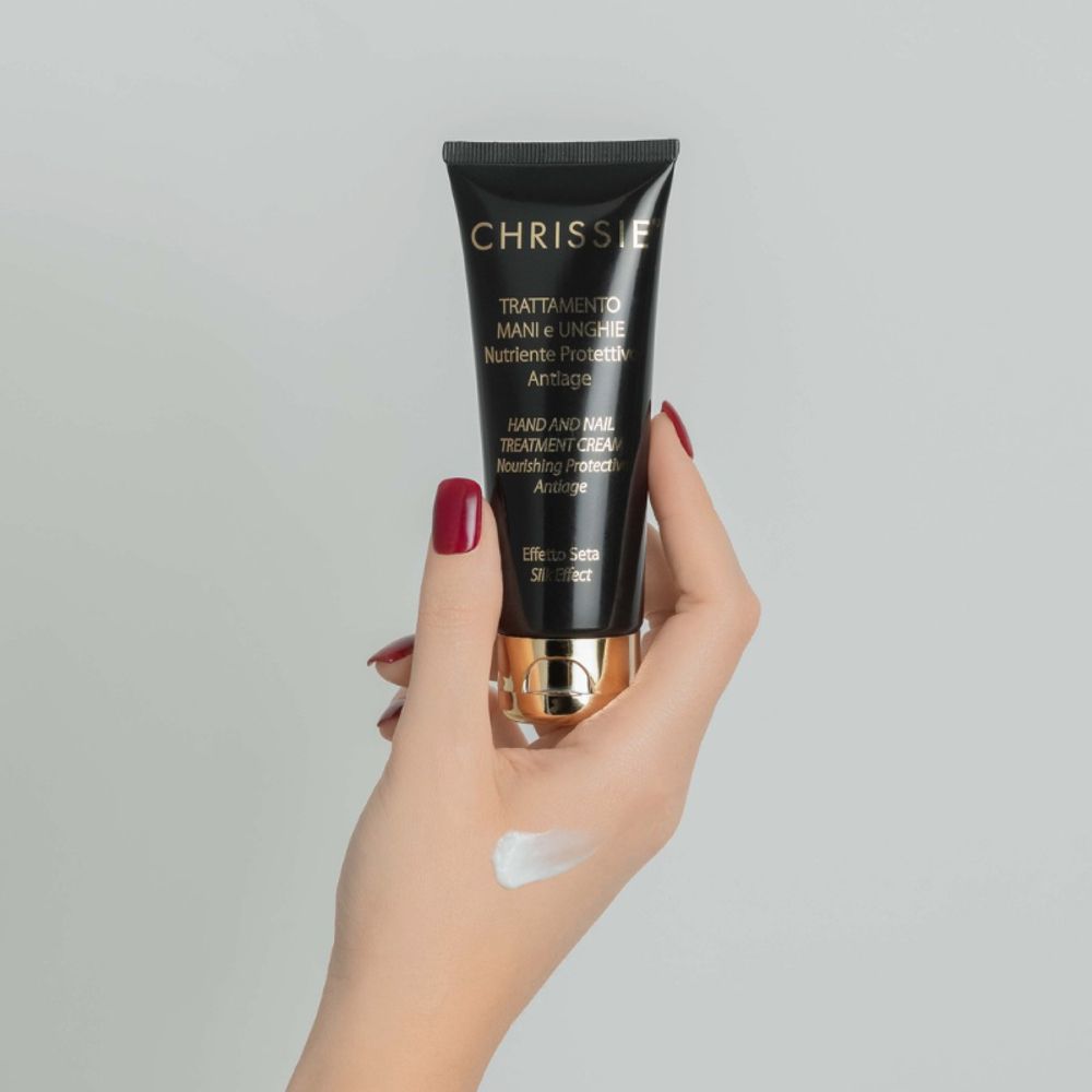 Mano che tiene il tubo. Crema sul dorso della mano. Tubo nero con tappo dorato. Testo: Chrissie, Trattamento Mani e Unghie.