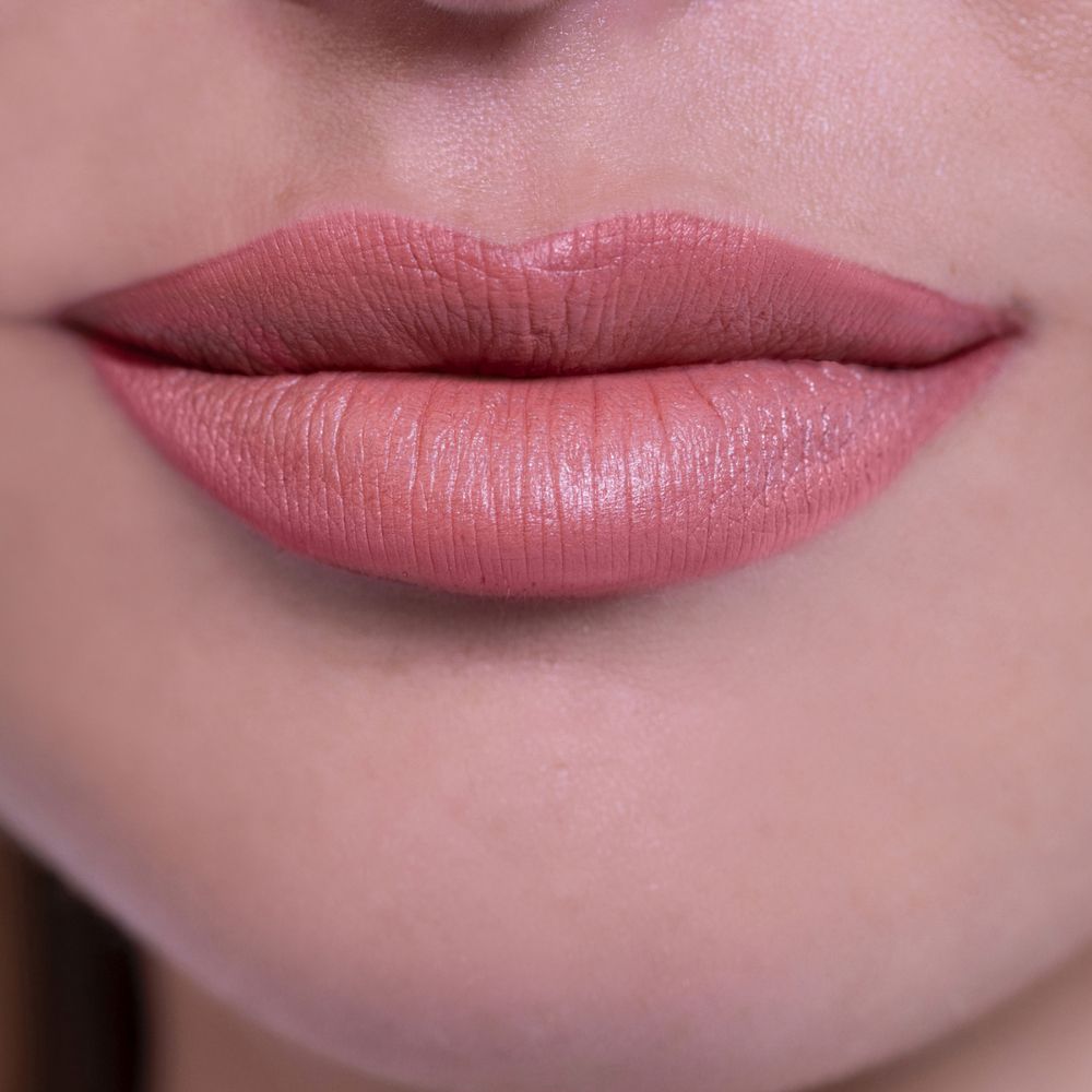 Primo piano di labbra truccate con rossetto nude chiaro. Texture liscia e cremosa.