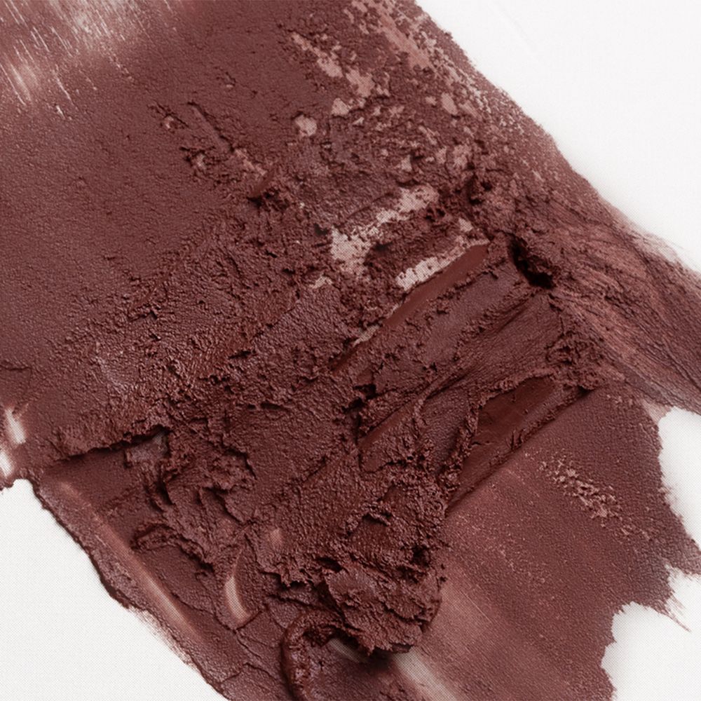 Primo piano di un campione di rossetto marrone su sfondo bianco. La texture è cremosa e irregolare.