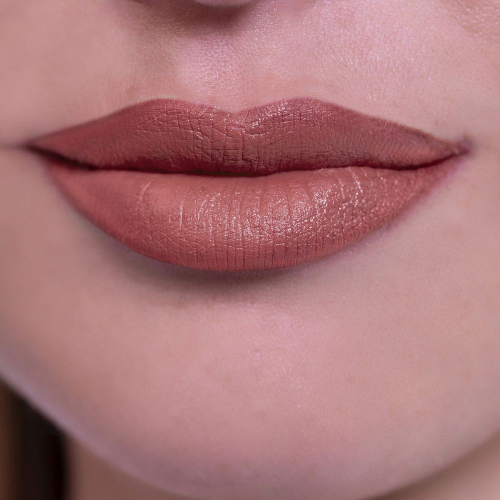 Primo piano di labbra dipinte con un rossetto marrone chiaro. Le labbra sono lisce e definite.