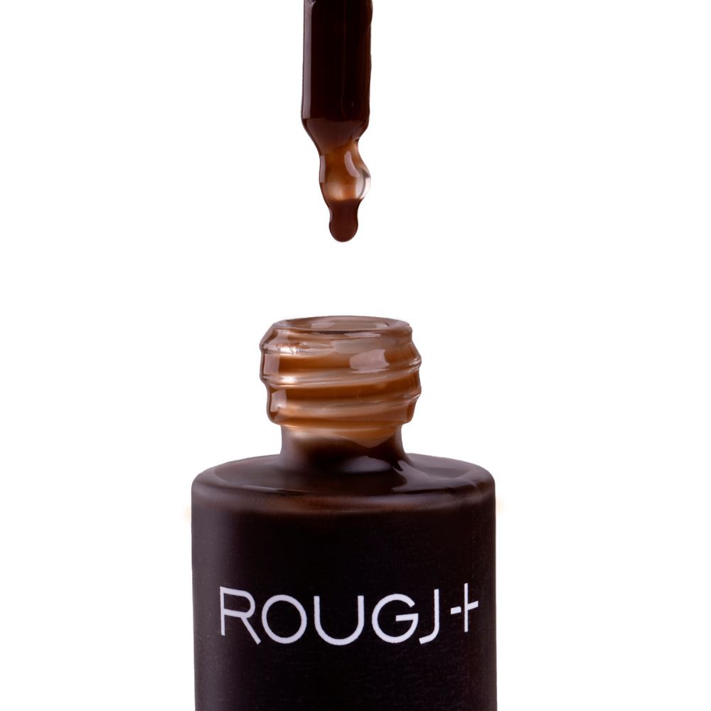 Primo piano dell'apertura di un flacone con gocce di liquido marrone. Scritta: ROUGJ+.