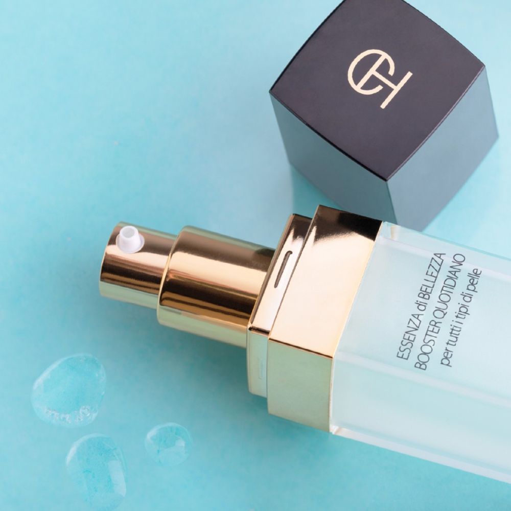 Flacone aperto con vaporizzatore. Scritta: Essenza di Bellezza Booster Quotidiano. Su sfondo blu.