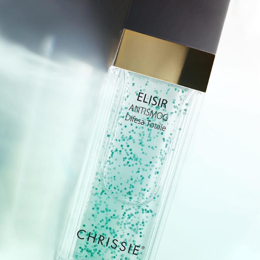 Primo piano del flacone con particelle verdi. Scritta: ELISIR ANTISMOG Difesa Totale, CHRISSIE.