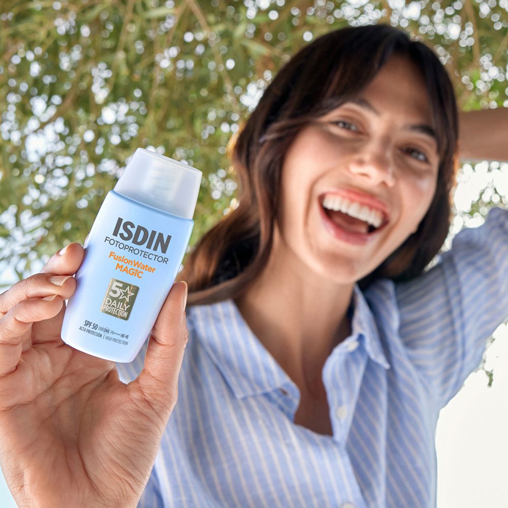 Donna che tiene in mano un flacone azzurro. Scritta: ISDIN Fotoprotector Fusion Water MAGIC. SPF 50. 5x Daily Protection.