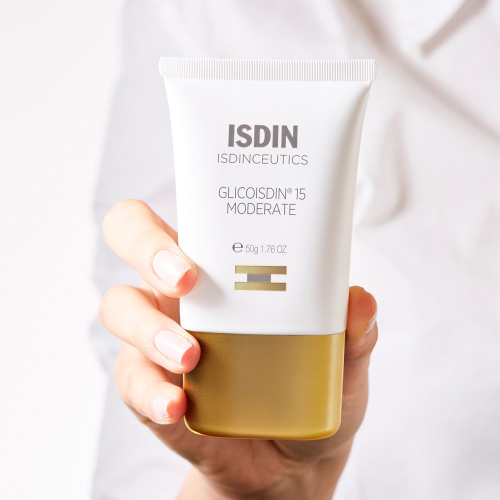 Tubo bianco ISDIN Glicoisdin 15 Moderate con base dorata, tenuto in mano. Testo: ISDIN, Glicoisdin 15 Moderate, 50g.