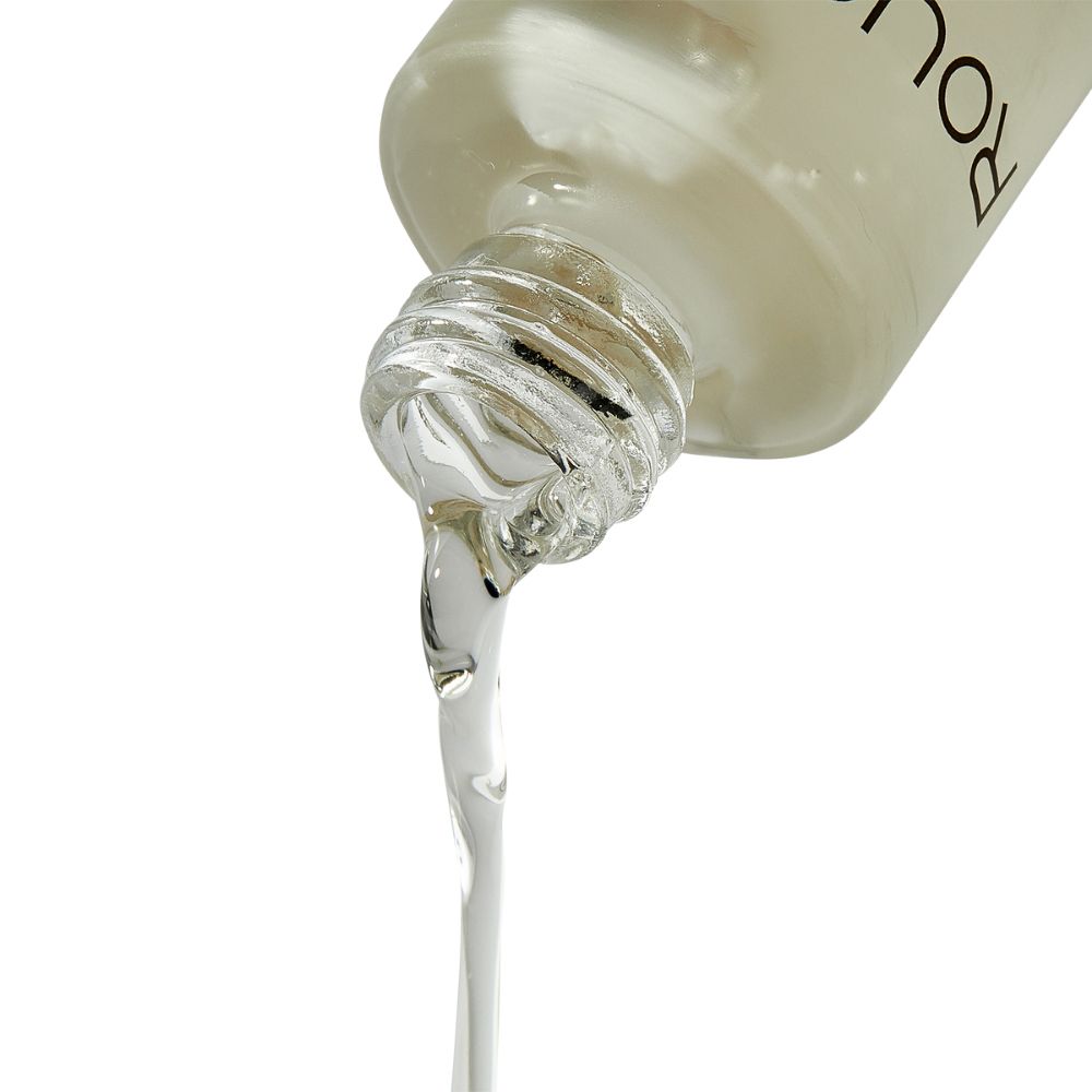 Liquido che esce da un flacone. Liquido trasparente e viscoso. Collo del flacone con tappo argentato.