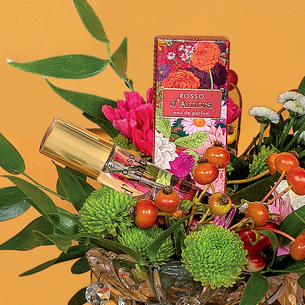 Flacone di profumo e scatola in decorazione floreale. Scritta: ROSSO d'Ambra, eau de parfum. Logo: HELAN.