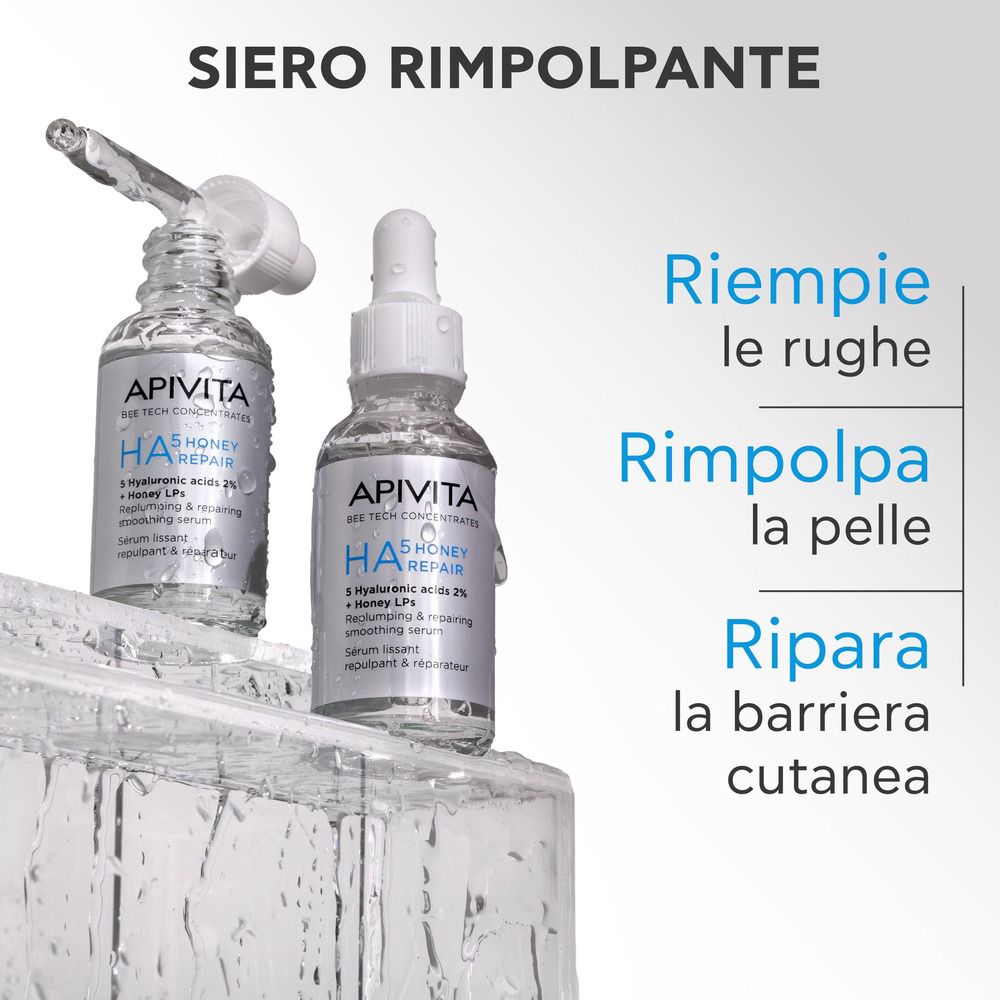 Due flaconi Apivita HA5 Honey Repair Siero Viso su blocchi di ghiaccio. Testo: Siero Rimpolpante. Testo in italiano.