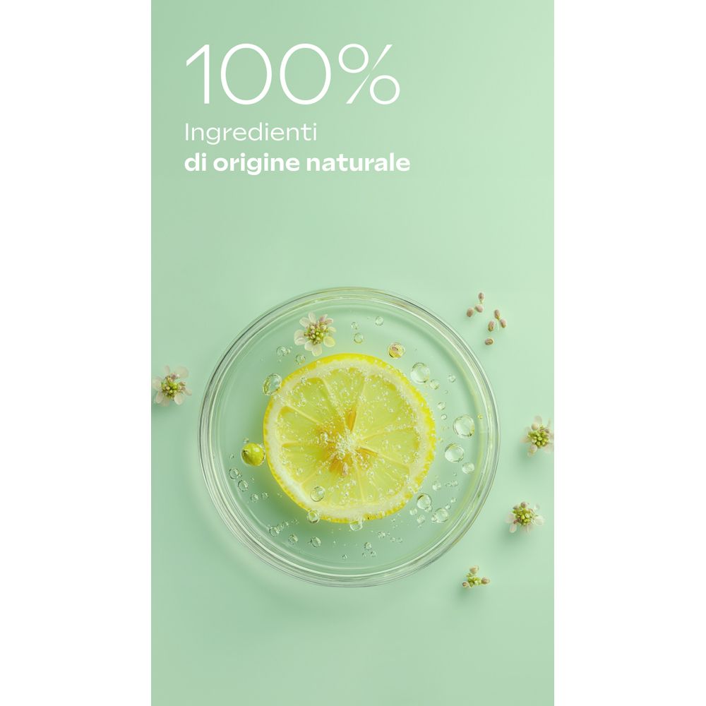Fetta di limone in una capsula di Petri con fiori e gocce d'acqua. Testo: 100% ingredienti di origine naturale.