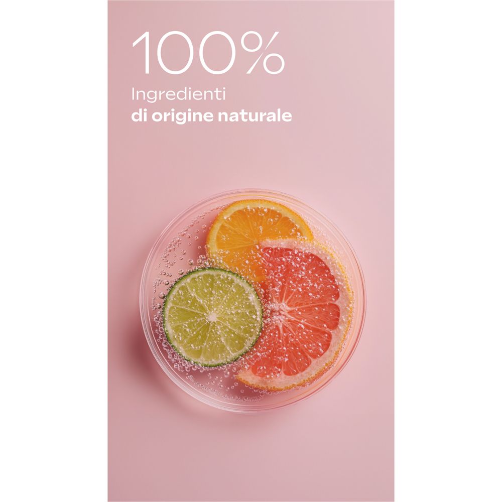 Su sfondo rosa, una capsula di Petri con fette di lime, arancia e pompelmo. Testo: 100% Ingrédients di origine naturale.