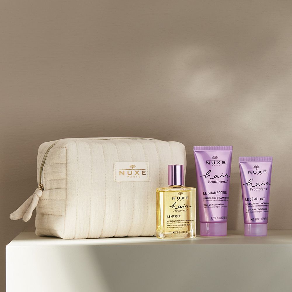 Beauty case con prodotti per capelli su un ripiano. Contiene olio, shampoo e balsamo. Logo Nuxe visibile.