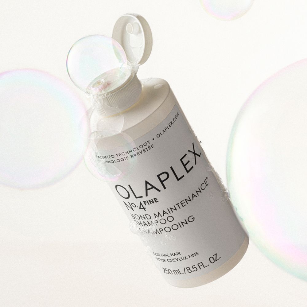 Flacone bianco di shampoo circondato da bolle di sapone. Olaplex No.4 Bond Maintenance Shampoo.