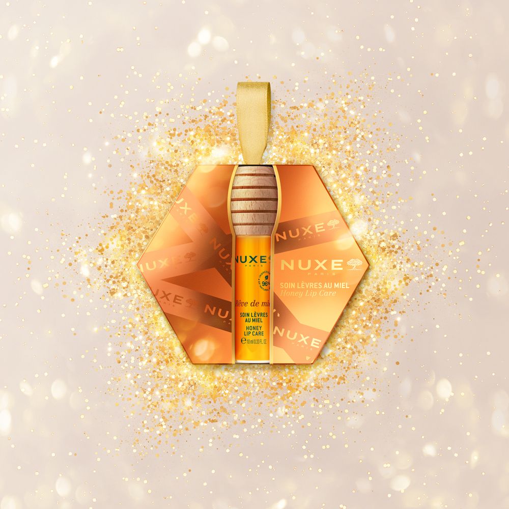 Confezione regalo esagonale arancione con nastro dorato. Contiene un balsamo labbra. Sfondo dorato con glitter.