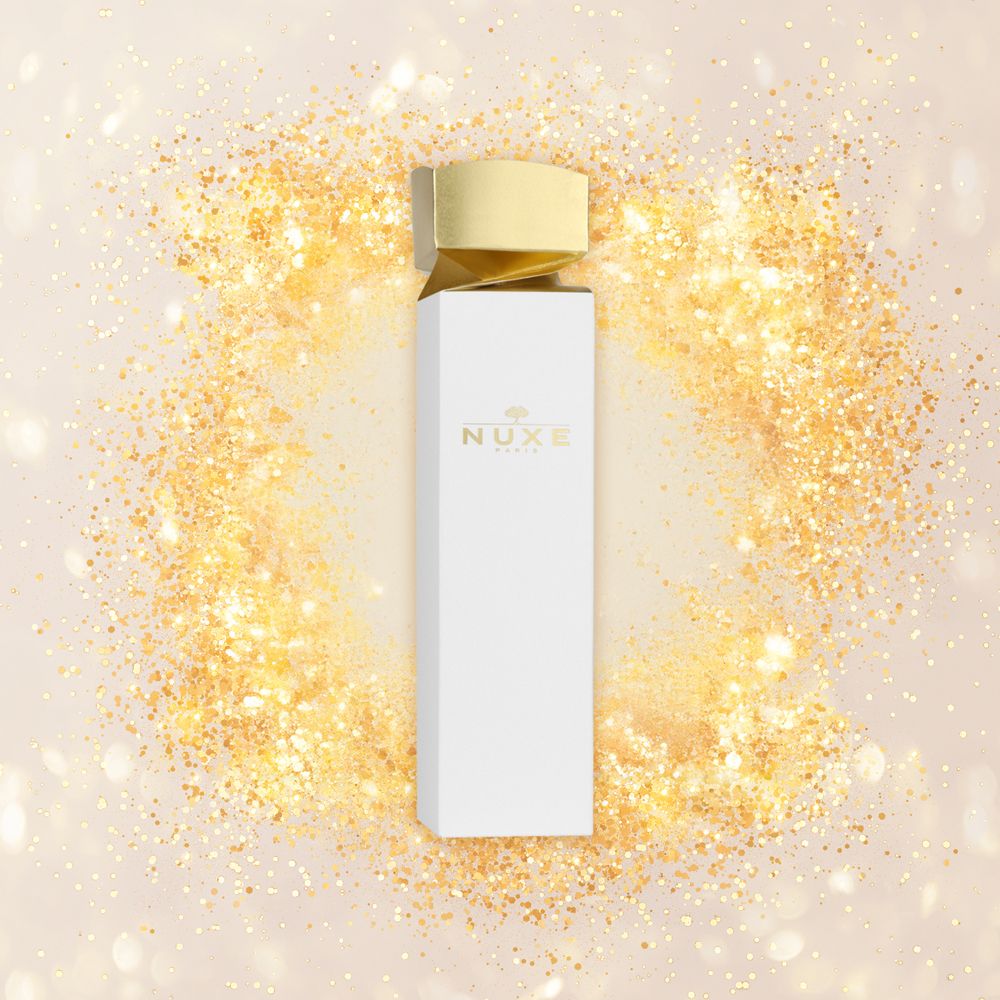 Confezione regalo bianca e dorata su sfondo di coriandoli dorati. Logo Nuxe. Coperchio dorato.