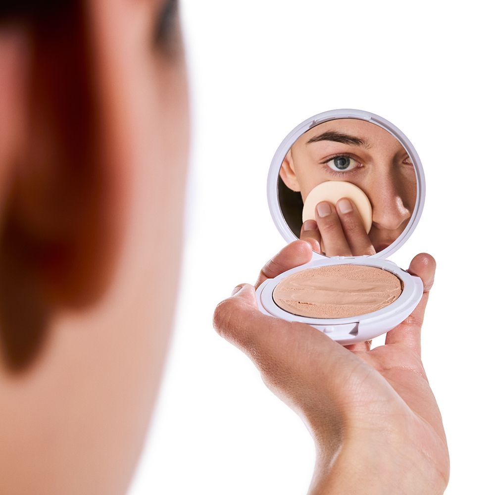 Persona che tiene crema CC compatta con specchio. Applicazione del prodotto con spugna. Nome prodotto: Compact Touch CC Cream.