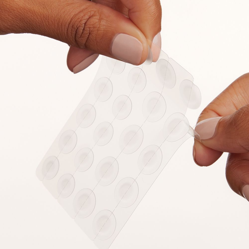 Mani che staccano cerotti CeraVe trasparenti da un foglio. Forma rotonda.