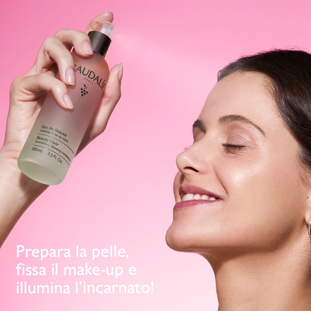 Donna spruzza Caudalie Eau de Beauté sul viso. Testo: Prepara la pelle, fissa il make-up e illumina l'incarnato!