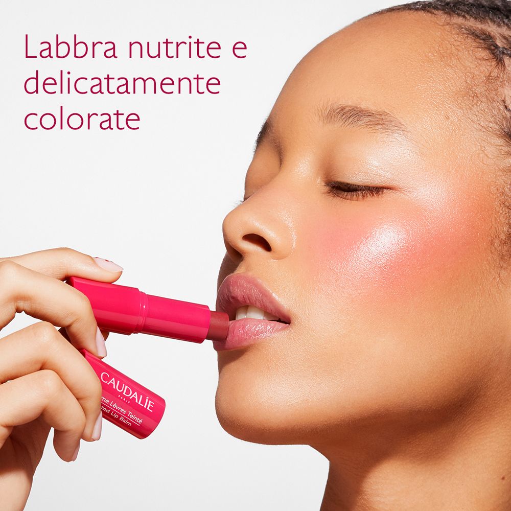 Donna applica balsamo labbra. Prodotto e logo Caudalie visibili.