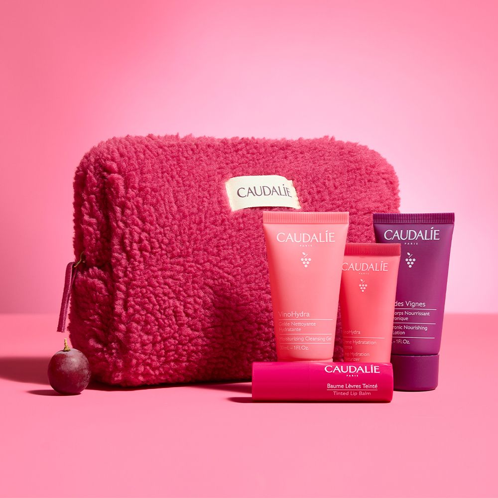Trousse rosa con prodotti Caudalie. Uva accanto. Sfondo rosa.