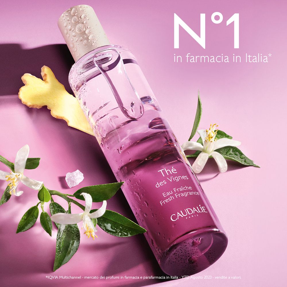 Flacone con liquido. Scritta: Thé des Vignes. Logo Caudalie. Fiori e zenzero accanto. Sfondo rosa.