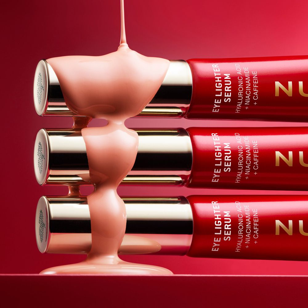 Tre tubi di Eye Lighter Serum, il siero scorre dai tubi. Sfondo rosso.