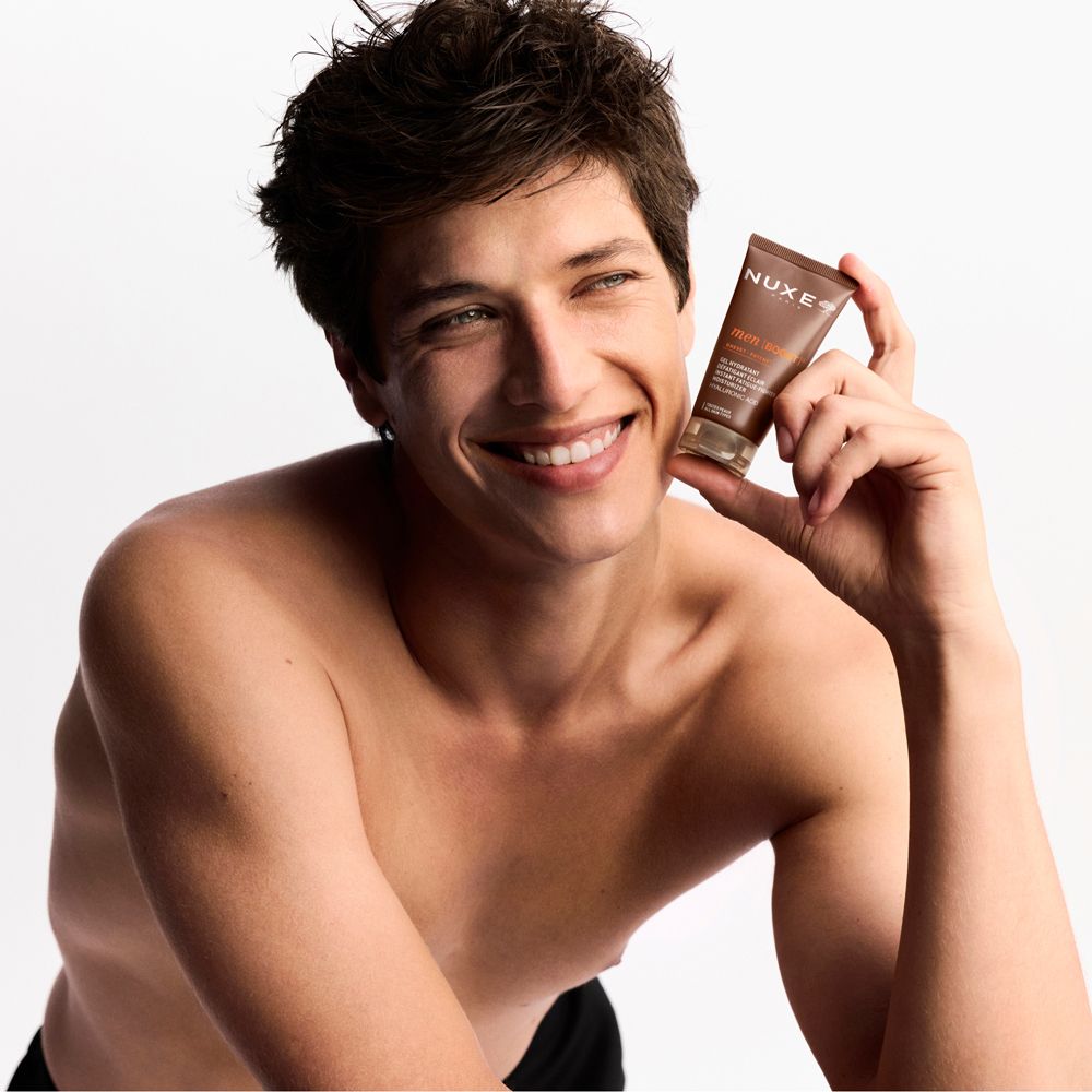 Uomo tiene tubo Nuxe Men [BOOST]. Sorride. A torso nudo.