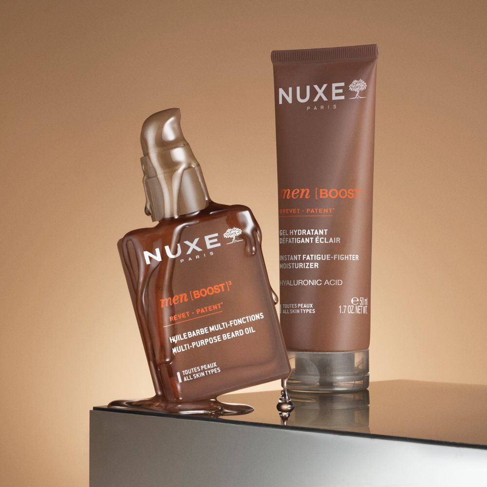 Prodotti Nuxe Men [BOOST]: flacone olio, gel e tubo. Su superficie lucida.