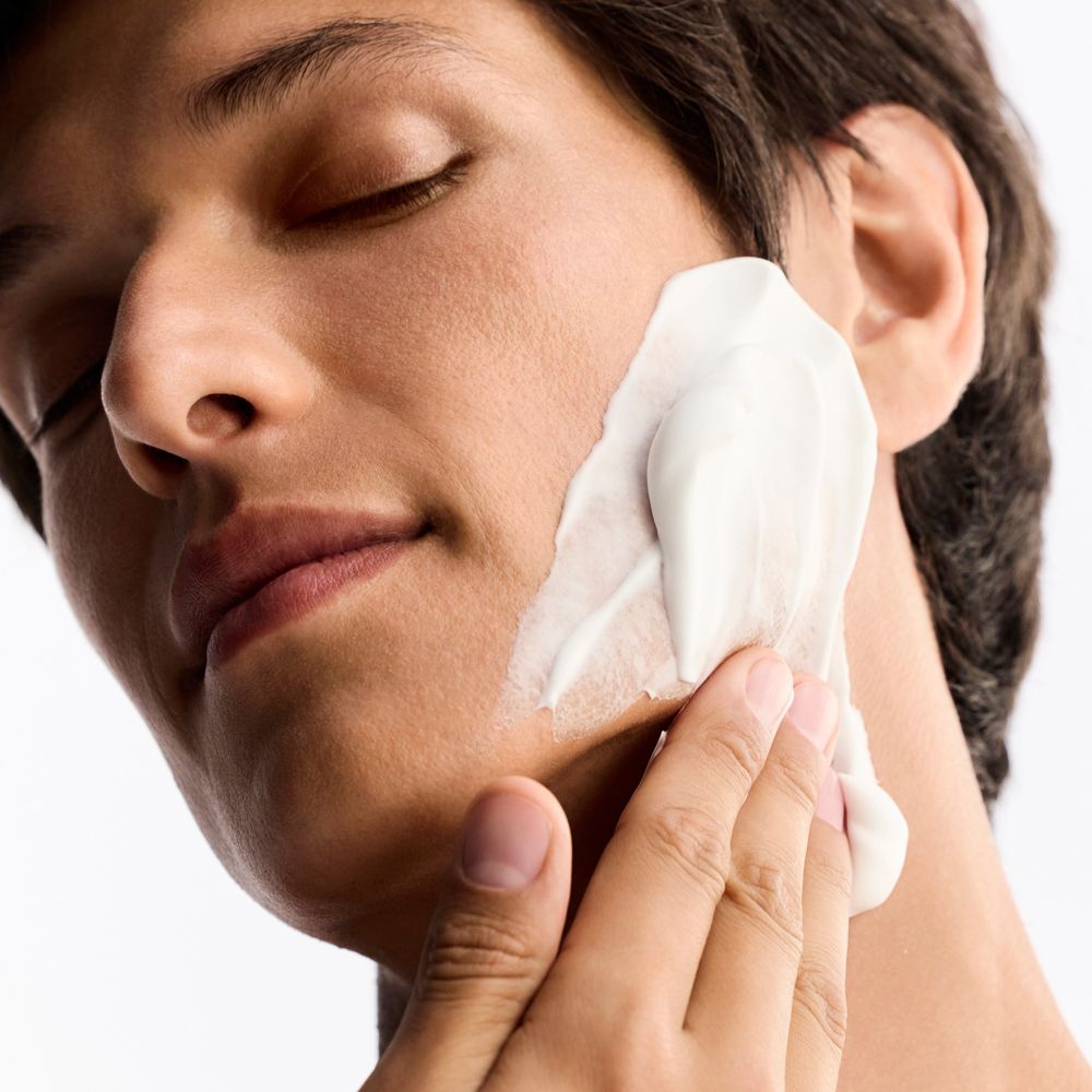 Uomo applica crema da barba sul viso. Crema bianca sulla guancia. Occhi chiusi.