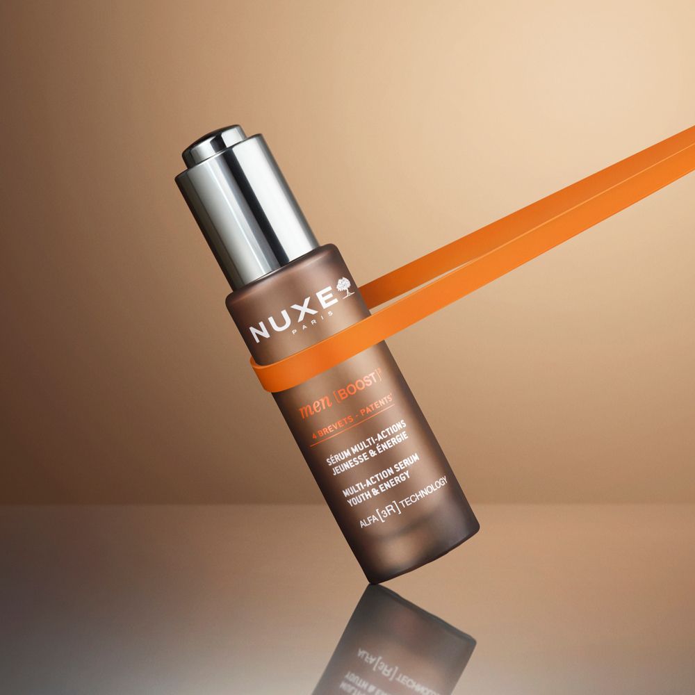 Flacone di vetro marrone con tappo argentato, tenuto da un nastro arancione. Scritta: Nuxe Paris, Men Boost.