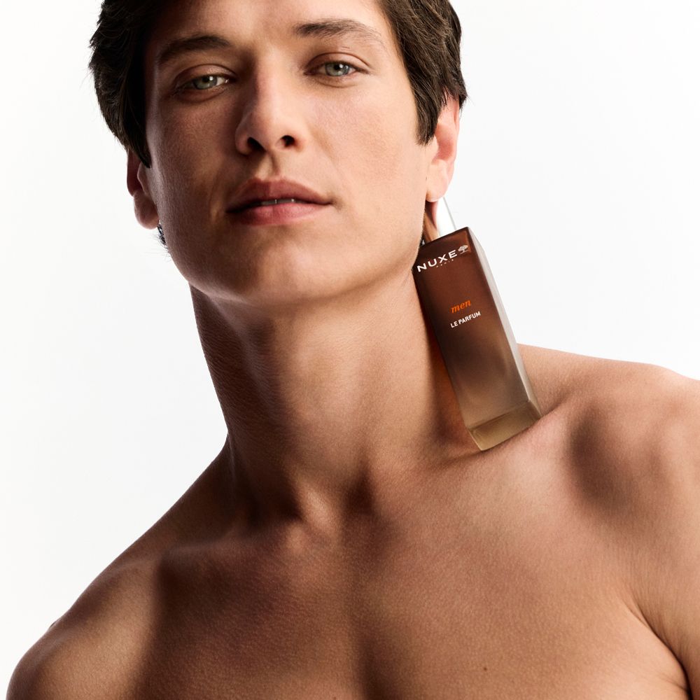 Uomo con flacone in vetro marrone al collo. Scritta: NUXE Paris, men, LE PARFUM.