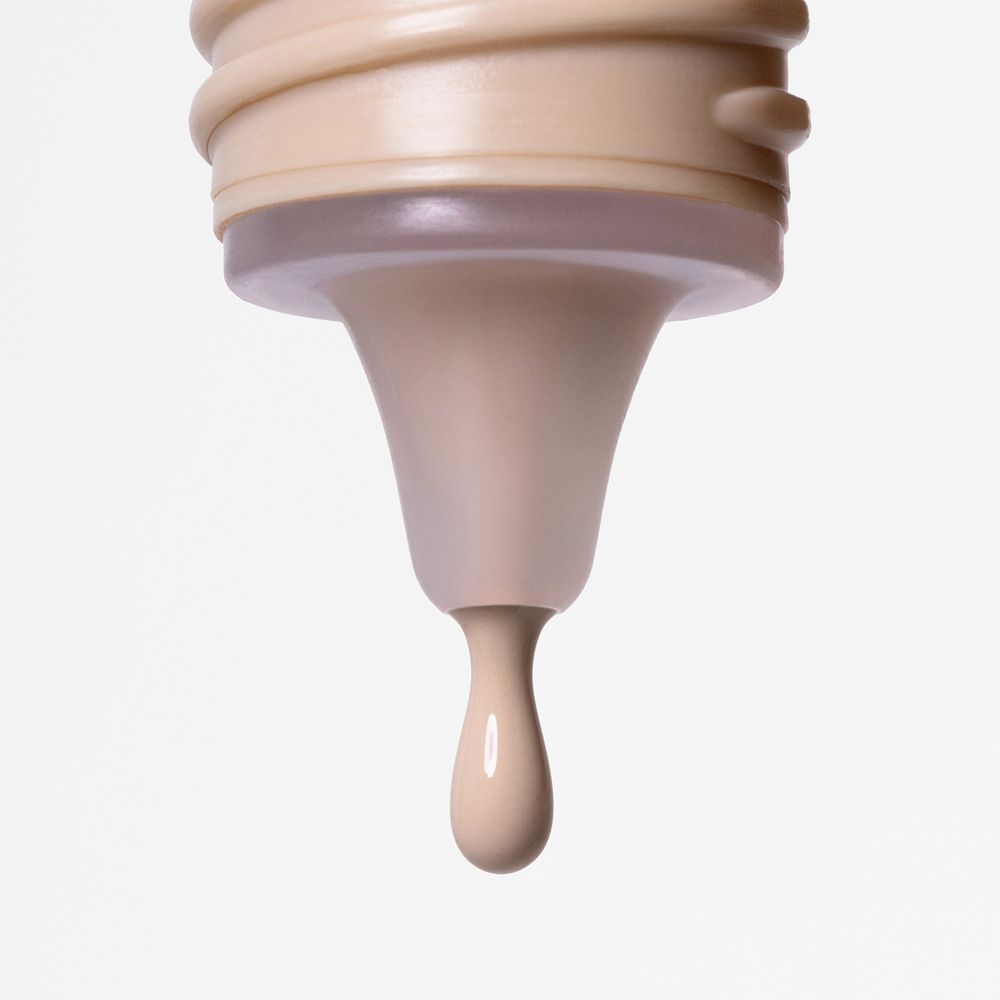 Primo piano dell'apertura di un flacone. Una goccia di fondotinta che cola. Colore beige.