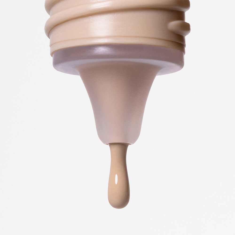 Primo piano della punta di un flacone. Una goccia di fondotinta che cola.