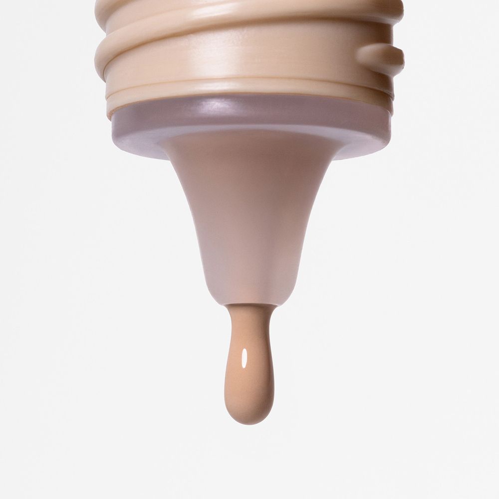 Primo piano dell'apertura di un flacone Astra Filter Drop Skin Tint. Una goccia di fondotinta cade.