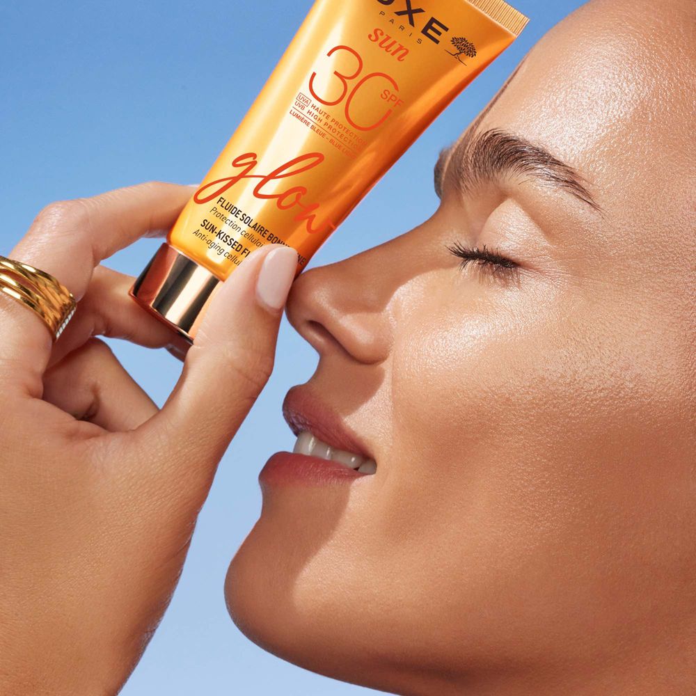 Donna tiene tubo Nuxe Sun, SPF 30, Glow. Primo piano del viso. Tappo dorato. 