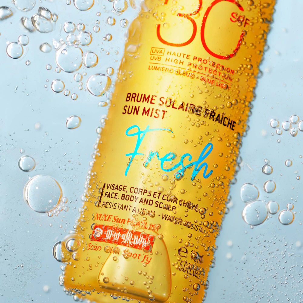 Flacone spray giallo-arancio con gocce d'acqua. Scritta: NUXE Sun, SPF 30, Sun Mist Fresh. Per viso, corpo e capelli.