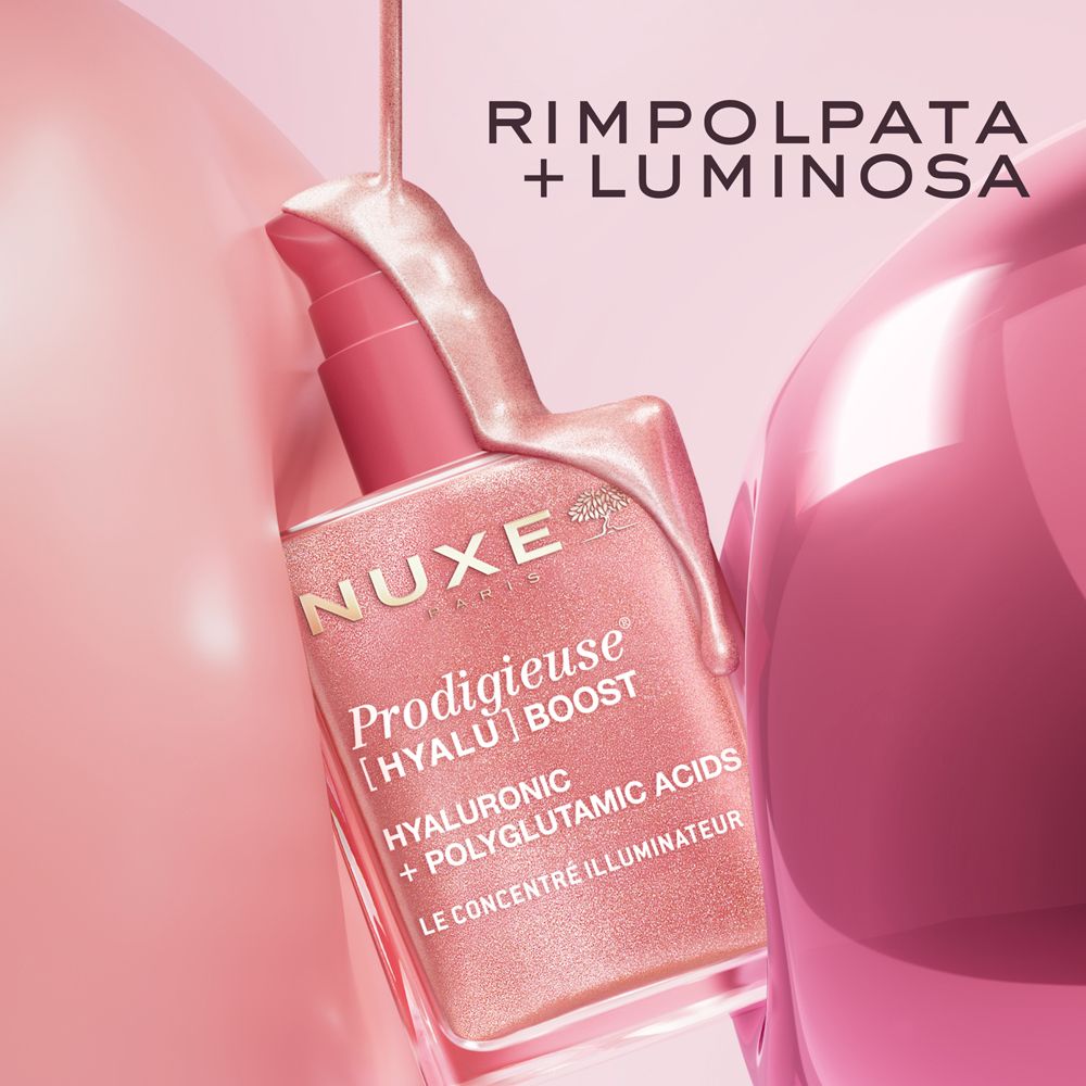 Liquido del prodotto che esce da un flacone. Scritta: Nuxe Prodigieuse [Hyalu] Boost. Sfondo rosa.