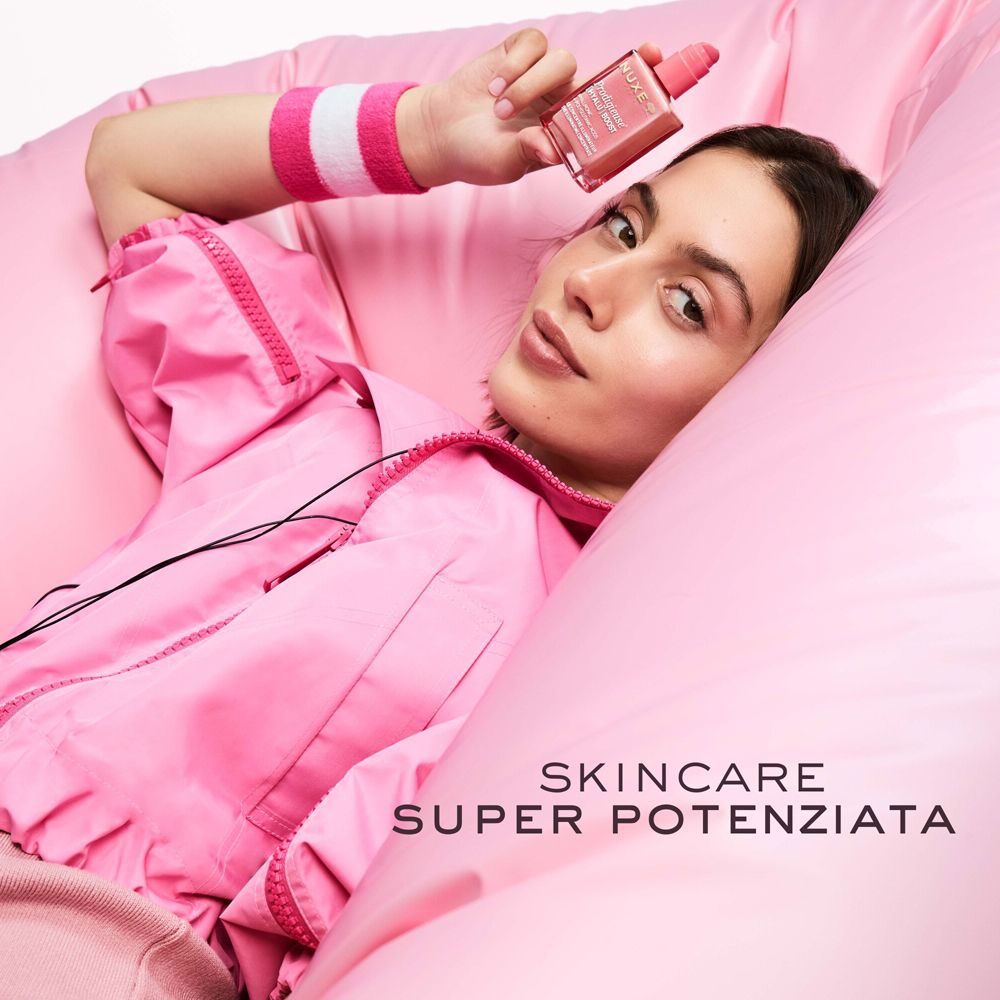 Donna su cuscino rosa. Tiene un flacone. Testo: Skincare Super Potenziata.