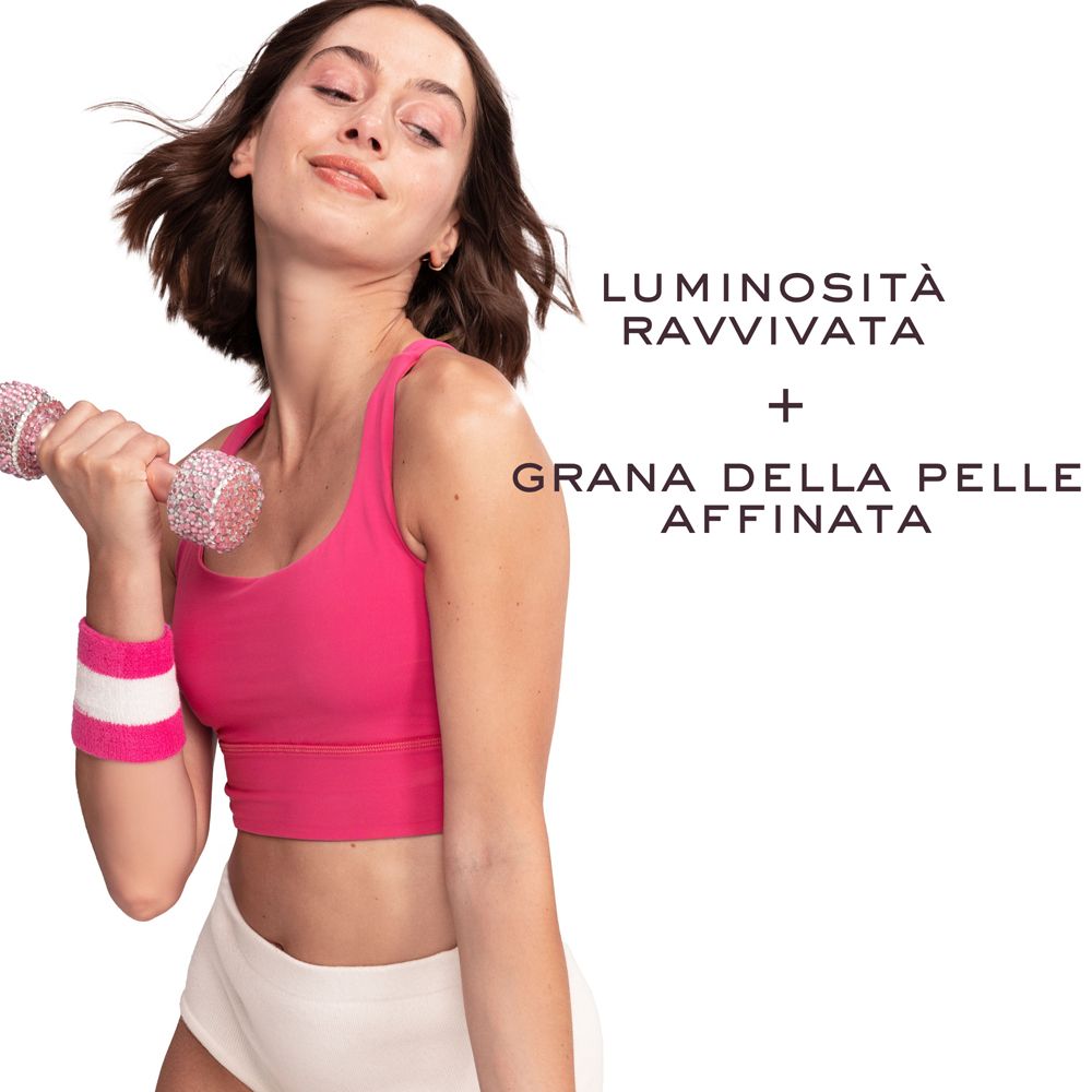 Donna in abbigliamento sportivo che tiene un manubrio rosa. Testo: Luminosità Ravvivata + Grana della Pelle Affinata.