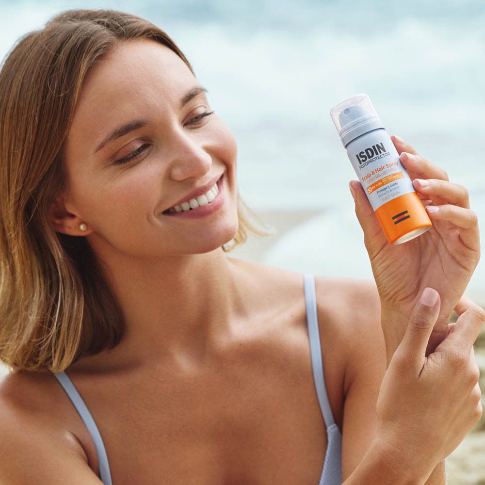 Donna tiene un flacone spray. ISDIN Fotoprotector Scalp & Hair Spray SPF50. In spiaggia. Protezione solare per capelli.