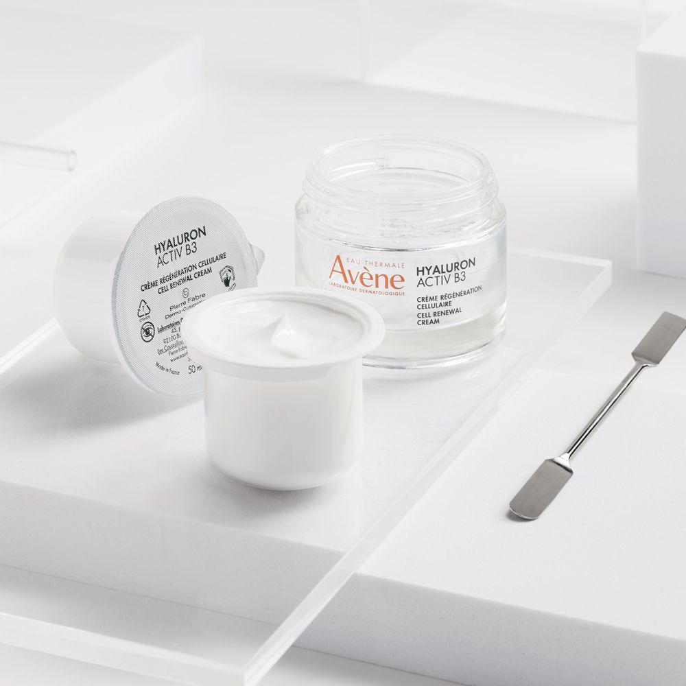 Crema Rigenerazione Cellulare Hyaluron Activ B3 Avène: vasetto aperto, piccolo campione e spatola su sfondo bianco.