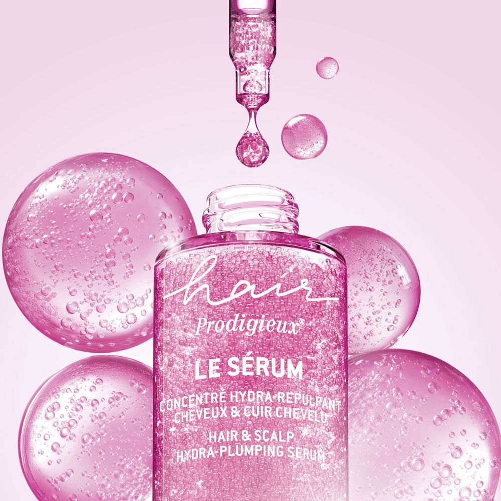 Flacone in vetro rosa con pipetta, circondato da bolle rosa. Scritta: Hair Prodigieux Le Sérum.