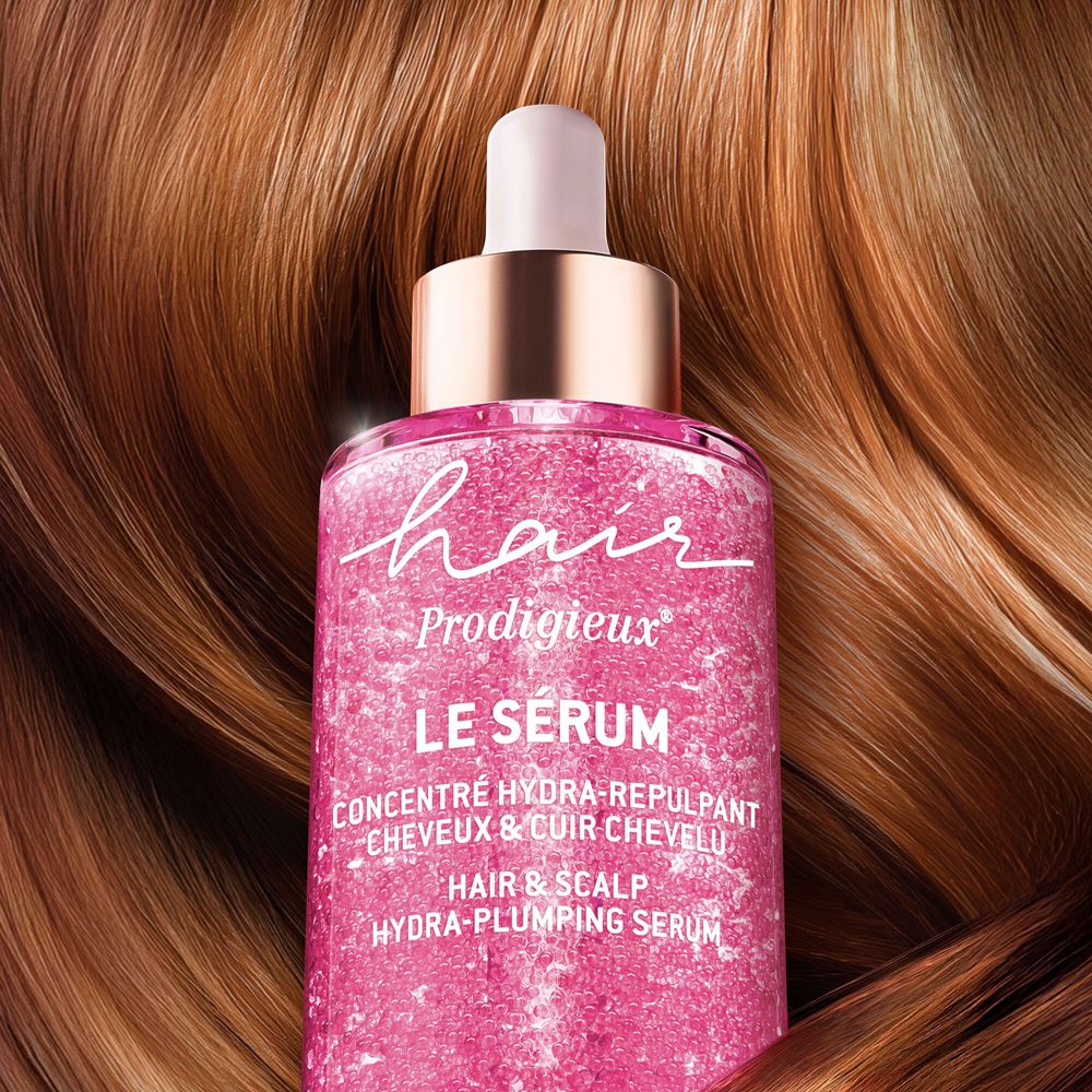 Flacone in vetro rosa davanti a capelli castani. Scritta: Hair Prodigieux Le Sérum.