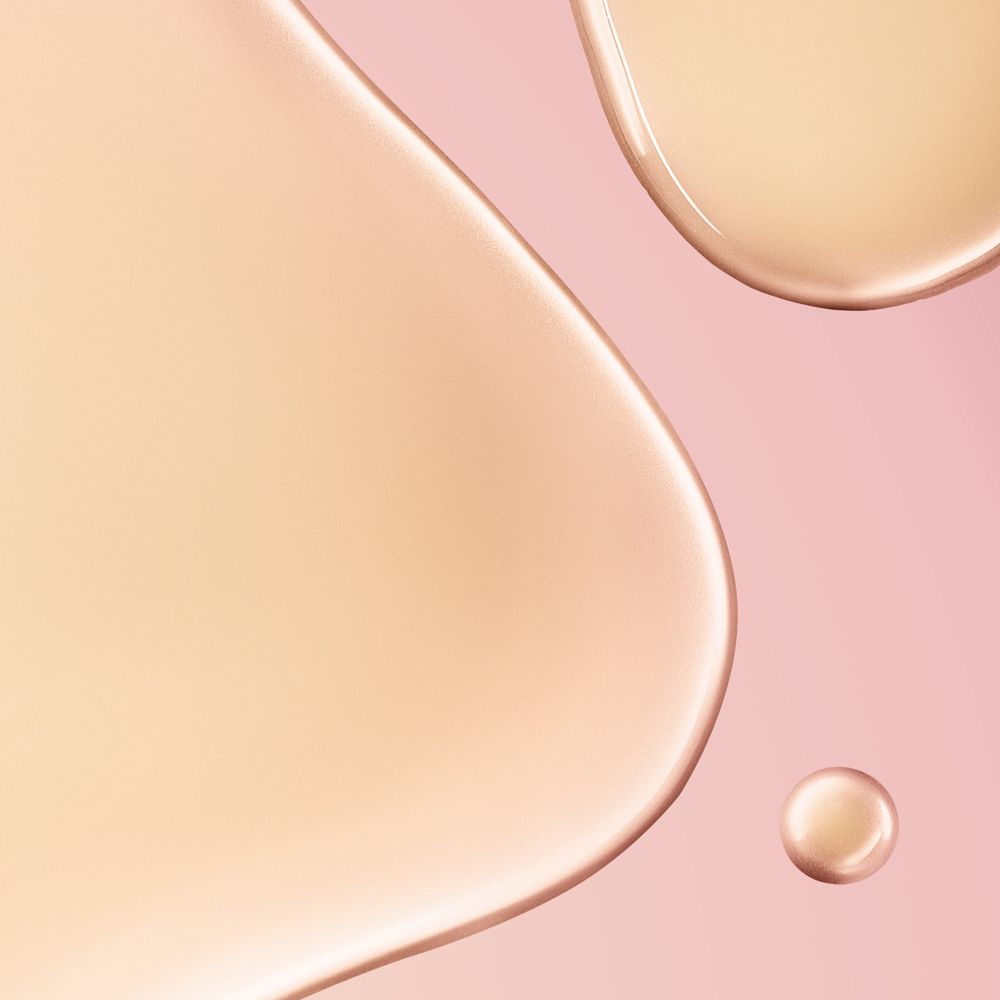Primo piano di gocce di liquido. Sfondo rosa. Il liquido è marrone chiaro e traslucido.